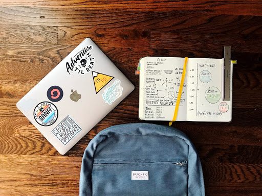 A laptop, a notebook, and a backpack lie on the floor